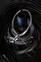 Metallic brake and gear cables coiled into loops and hanging on a hook in a bicycle mechanic s workshop. Focus on cycling maintenance, tools, and repair equipment.