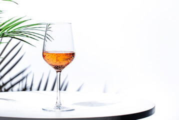 Non-alcoholic, alcohol free, pink rose wine pinot noir in glass. White background, palm leaves shadows, hard light