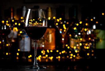 Italian dry red wine sangiovese in glass and wine bottles on dark bar background with lights
