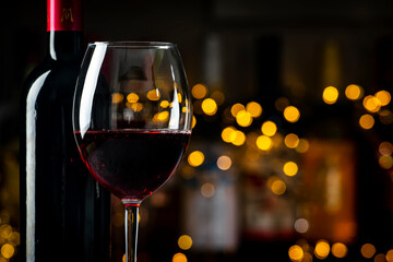 Dry red wine Cabernet Sauvignon in glass and wine bottle on dark bar background with lights