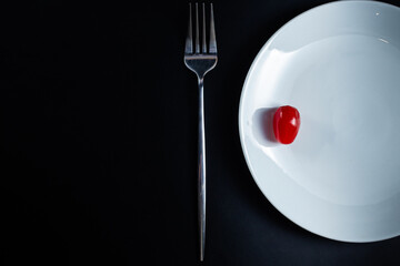 tomato on white plate with knife and fork on black background