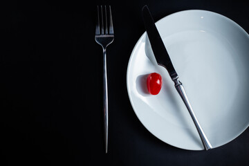 tomato on white plate with knife and fork on black background