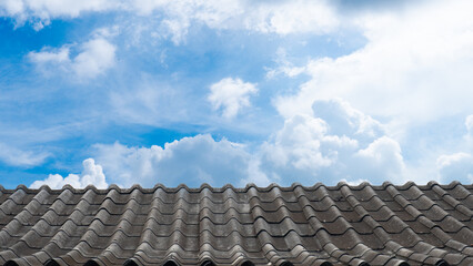 Vintage gray tiled roof against a backdrop of a bright blue sky dotted with fluffy white clouds. Perspective is from a slightly lower angle looking up at the roof and the sky.