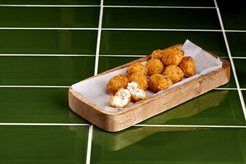 Deep fried cheese balls resting on wooden tray with parchment paper on green tiled surface