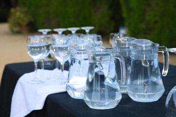 group of pitchers and crystal glasses with water on a black tablecloth on a catering table.
