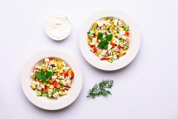 Fresh crab stick salad with cucumber, dill, eggs, corn and homemade mayonnaise sauce on light table top view. 