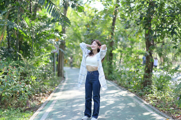 Asian woman enjoys summer, breathing fresh air on lush green pathway, surrounded by vibrant trees...
