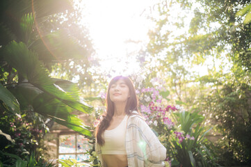 woman enjoys sunlight in lush garden surrounded by vibrant flowers and greenery, radiating peace...