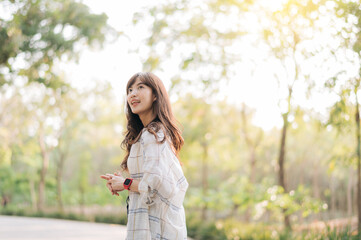 Asian woman enjoying summer outdoors, breathing fresh air in serene park with sunlight filtering...