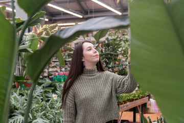 In a flower shop, a girl chooses flowers for decorating a house. The buyer looks at the flowers with curiosity, getting acquainted with the assortment of the trading platform