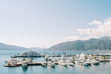 Expensive superyacht and motor yachts are moored to piers in the sea against the backdrop of mountains