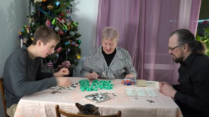 An elderly old woman pensioner plays Bingo. A grandmother with her family plays board games near Christmas tree at home. Lotto. Time together