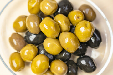 Black fermented olives and green olives preserved in close-up view on a bowl.