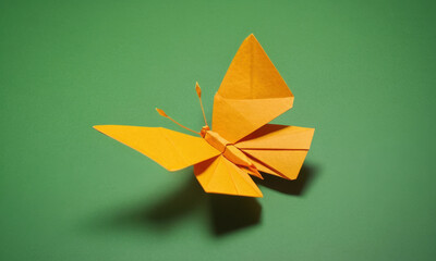 A delicate yellow origami butterfly perched on a green surface