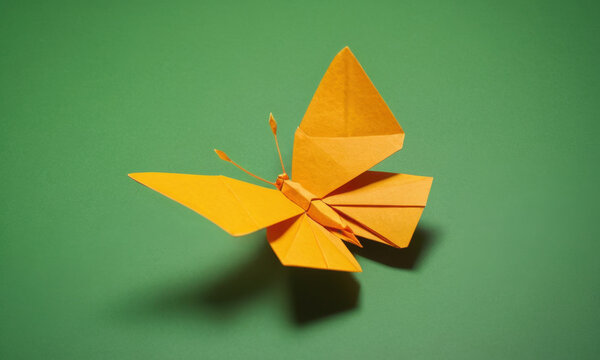 A delicate yellow origami butterfly perched on a green surface