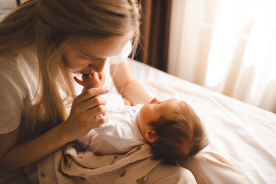 Mother kissing baby fingers holding on hands in bed close up. Motherhood.