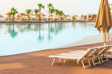 Sun loungers and umbrella by the pool with clear azure water in the tropics