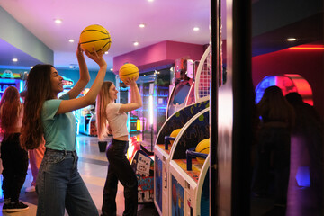 Two friends playing a basketball arcade game in an amusement park, having fun and enjoying their leisure time