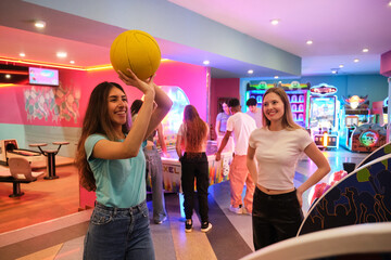Two friends playing arcade basketball with other young people having fun in the background
