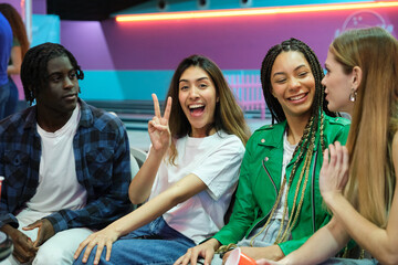 Young people enjoying time together at bowling club, gesturing victory sign and laughing
