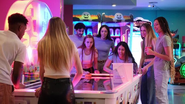 Group of young people having fun together playing air hockey in a colorful amusement arcade