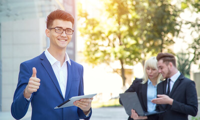 Man reading the news on his digital tablet. Asian business man on background of its employees outside the office. 
