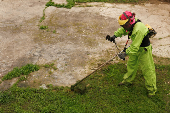 Mujer con mono verde de trabajo y protecciones de seguridad con una desbrozadora  cortando la hierba 