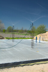 Budowa domu, pielęgnacja świeżej płyty fundamentowej poprzez zraszanie betonu wodą © gpmax