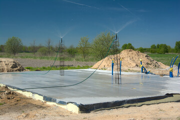 Budowa domu, pielęgnacja świeżej płyty fundamentowej poprzez zraszanie betonu wodą © gpmax