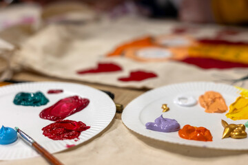 Acrylic paints on paper plates for fabric painting workshop, creative art process with colorful palette and brush.