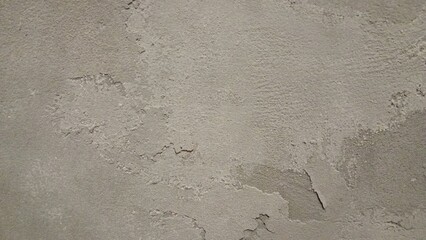 A close-up of a rough, worn-out concrete wall with a gritty texture, featuring cracks and crevices. The color is a dull, muted gray with subtle variations in shade, showing off the uneven surface.