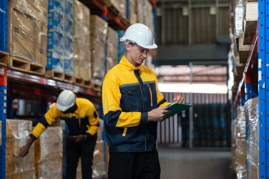 Man warehouse worker wearing uniform and helmet safety with clipboard for checking stock products on shelves in warehouse. Logistics, Distribution Center concept