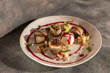 Rolled crepes with chocolate filling, garnished with mint, banana, crushed nuts, raspberry sauce, and served with vanilla ice cream on a dessert plate.