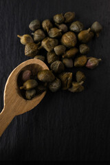 Capperi in cucchiaino di legno su fondo nero.