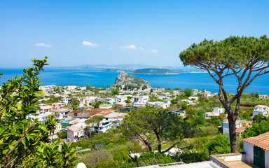 Scenic view of Ischia island with the historic Aragonese Castle, colorful houses, lush greenery, and the blue waters of the Gulf of Naples on a clear sunny day in Campania, southern Italy.