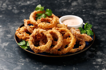 Homemade deep fried onion rings on plate with sauce.