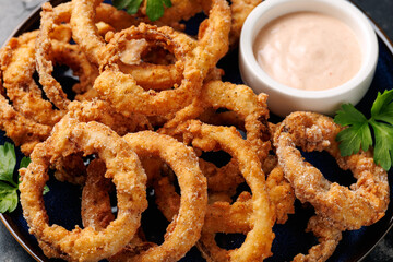 Homemade deep fried onion rings on plate with sauce.