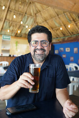 Smiling hispanic man enjoying a refreshing beer at a caribbean bar