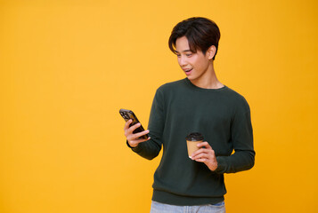 Happy excited young asian man using mobile phone isolated on yellow background. teen social media communication online.