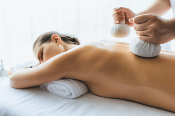 Hot herbal ball spa massage body treatment, masseur gently compresses herb bag on woman body....