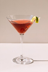 Close-up of a martini glass on a white table. An elegant goblet with a red alcoholic sparkling drink