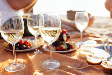 Close-up of a glasses of champagne on a picnic mat. The cups is filled with sparkling wine outdoors on the beach. Delicious snacks and berries by the sea.