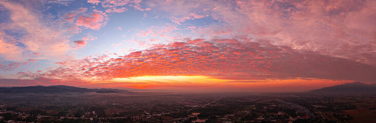 Fototapeta premium A breathtaking sunrise illuminates a small village nestled among lush green fields and karst mountains, with vibrant clouds filling the sky. The harmony of rural life set dramatic natural formations.