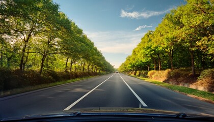 view from a car s dashboard through the windshield showing a long straight road flanked by trees