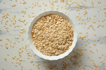 Oat grains in a white ceramic bowl and scattered on the table.