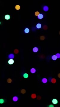 Una toma de cerca de varias luces de colores en forma de c&iacute;rculos en movimiento en la oscuridad. Desenfoque, efecto Bokeh. Video vertical