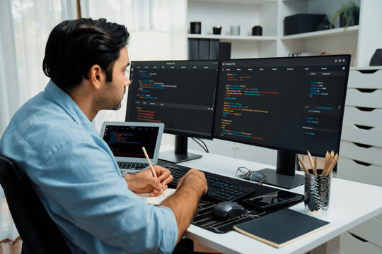 Smart IT developer writing data memo's software development on paper's coding on laptop and two pc screen, creating application program update version online website system at modern office. Surmise. - Powered by Adobe