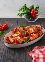 Step-by-step preparation of skewers on a skewer made of chicken, sweet pepper, bacon and onion on a light concrete background.