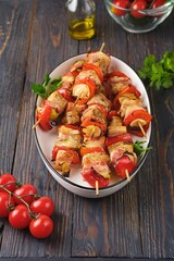 Step-by-step preparation of skewers on a skewer made of chicken, sweet pepper, bacon and onion on a light concrete background.