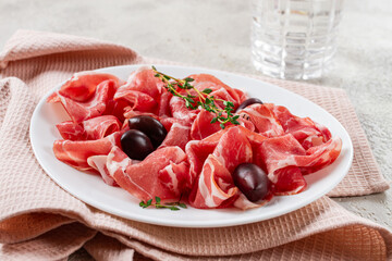 Freshly cut dried meat, served with olives and herbs, on a white plate, light background, no people,